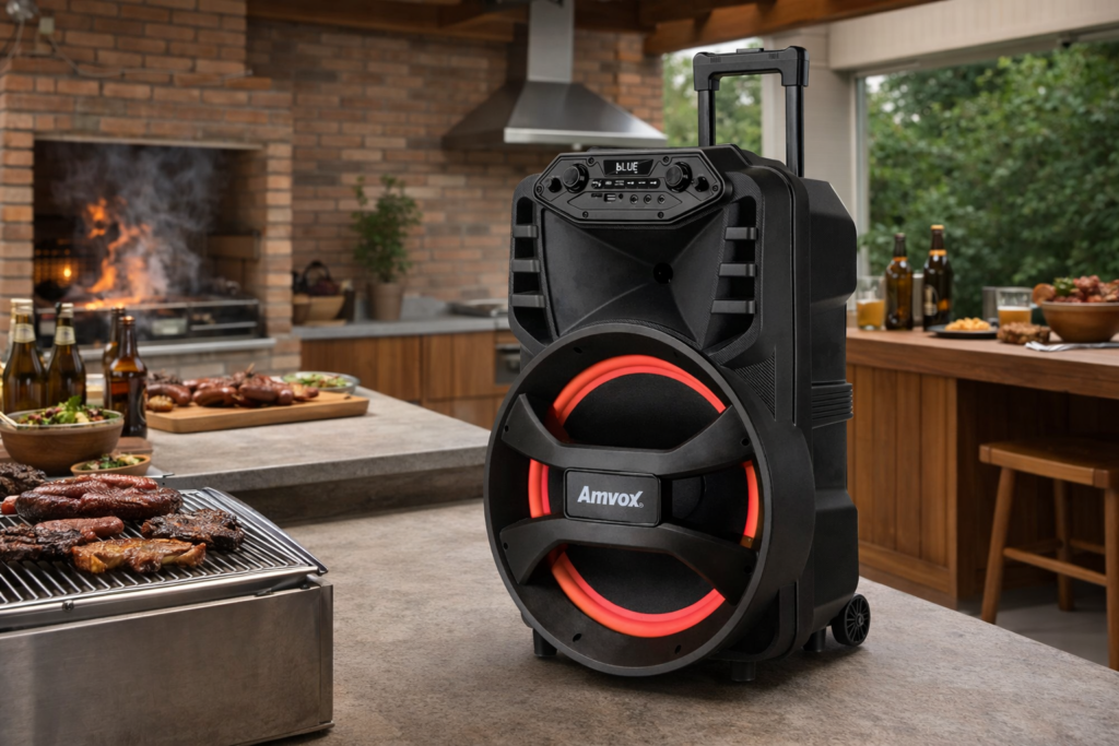 Caixa Amplificada Vegas ACA 880 posicionada em &aacute;rea gourmet com churrasqueira, sobre bancada de granito, ao lado de grelhados e bebidas, sob pergolado de madeira com luz natural.