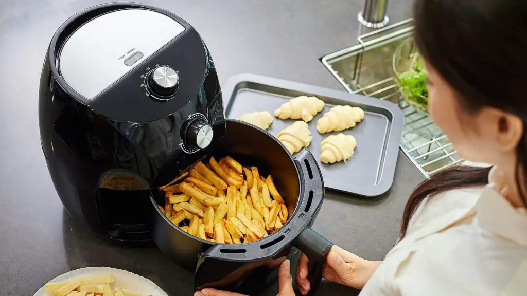 mulher retirando o cesto da air fryer após preparar uma porção de batata frita