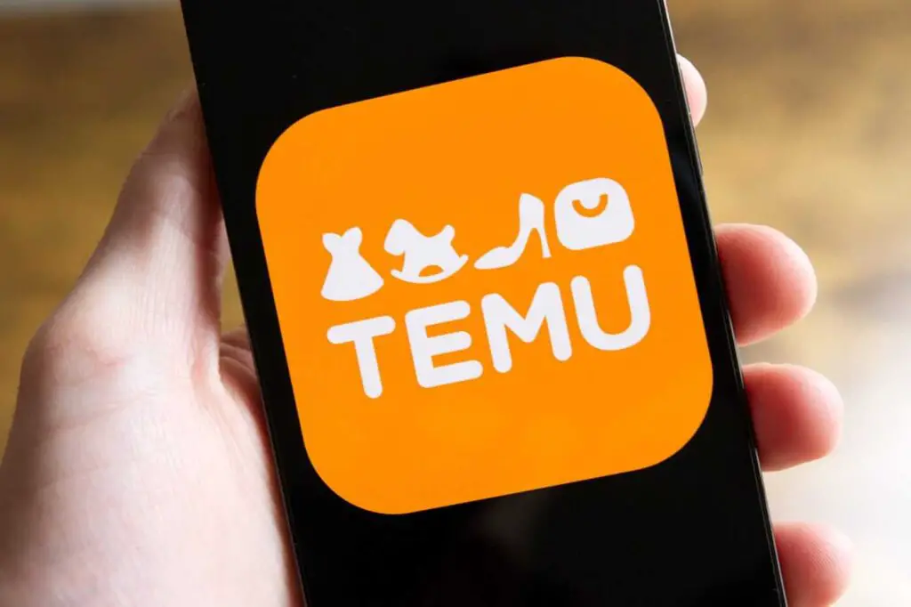 uma mão segura um celular ligado com o logotipo da Temu na tela