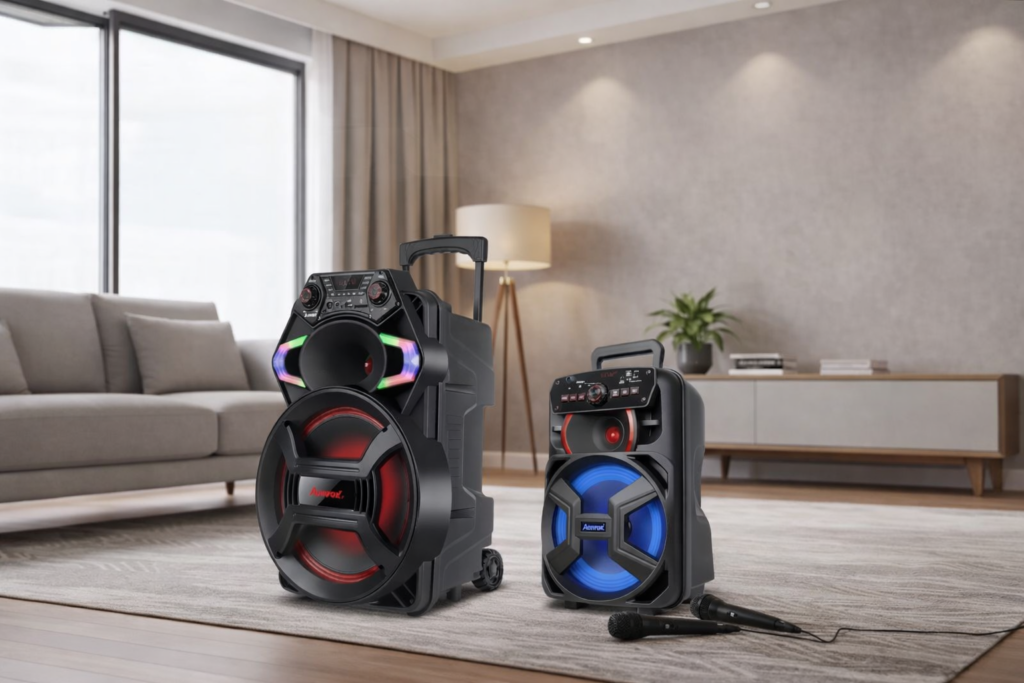 Duas caixas de som port&aacute;teis Amvox com luzes LED coloridas, uma maior e outra menor, posicionadas em uma sala de estar moderna com sof&aacute;, abajur e planta ao fundo.